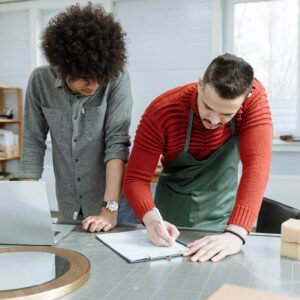 Two men working together at a desk, taking notes in a modern workshop environment.